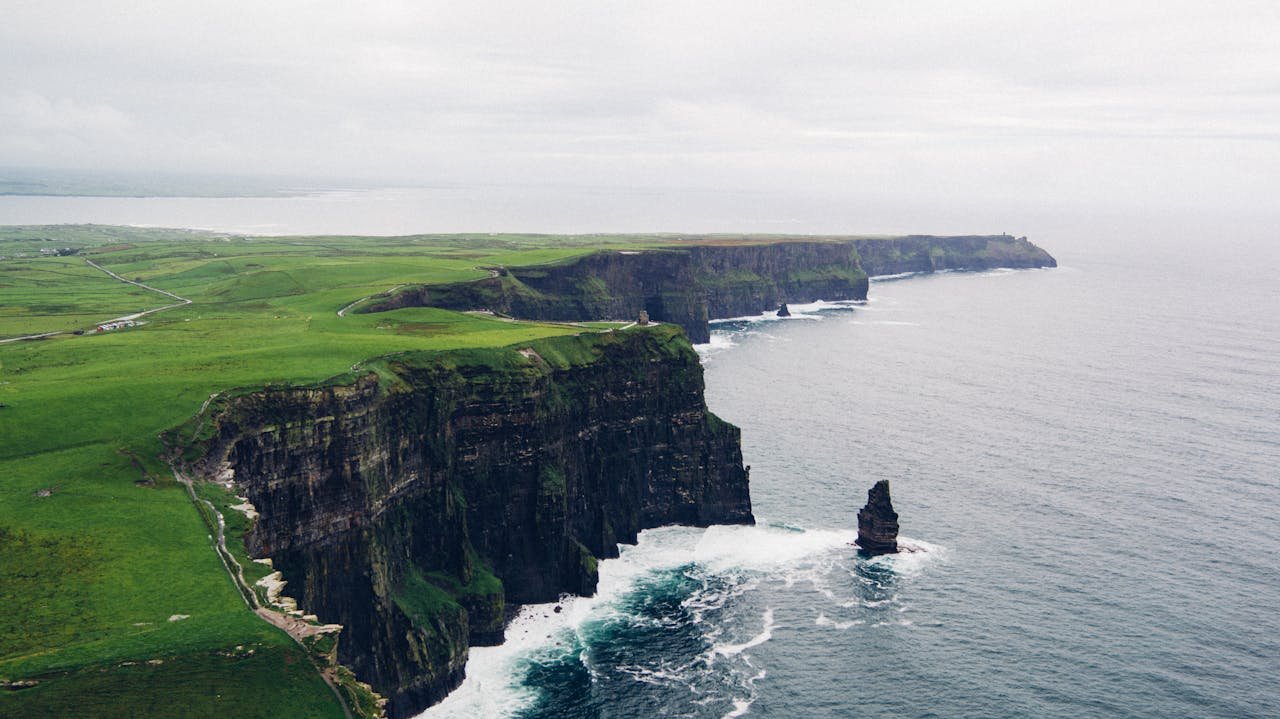 A breathtaking aerial view of the Cliffs of Moher with lush greenery and the Atlantic Ocean.